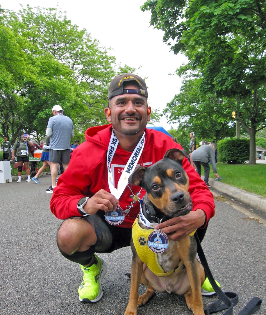 Jesus Flores, USMEPCOM command paralegal, and his dog Dino share a smile after finishing a 5K together. Flores, once 60 pounds heavier, now inspires others at USMEPCOM as a sharp-dressed ultra marathon runner.