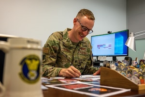 Service member signs paperwork at desk filled with coins.