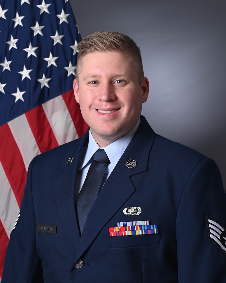 An official photo of SSgt Andrew Compton in front of the American flag wearing the service dress uniform.