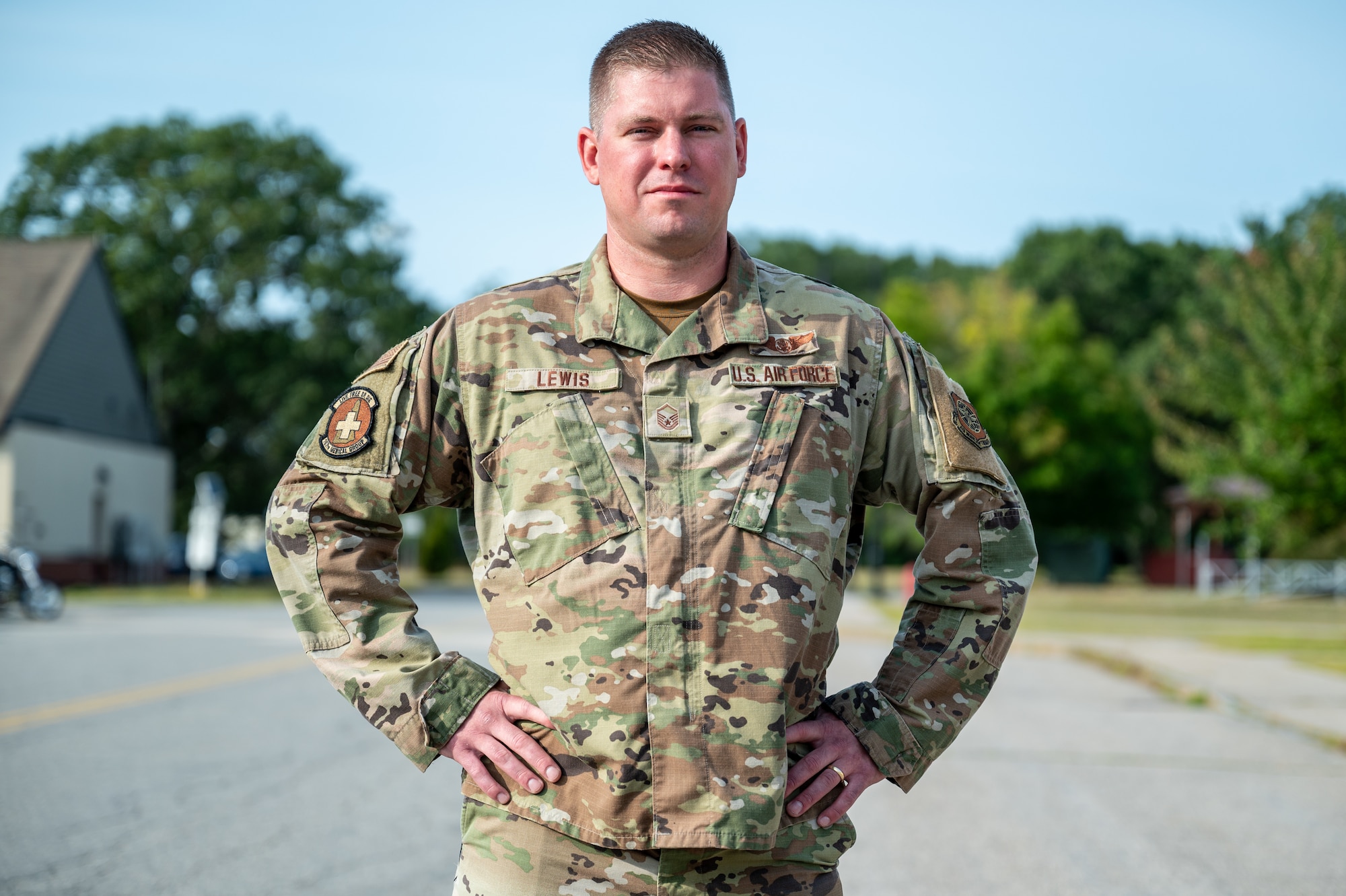 Airman stands outside in uniform, trees in background, clear blue sky