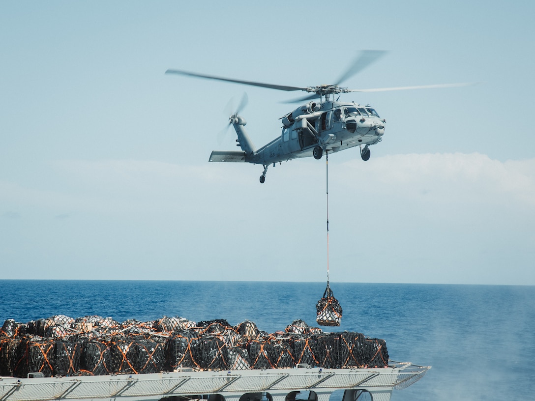A U.S. Navy MH-60S Seahawk Helicopter, assigned to Helicopter Combat Squadron 26, carries supplies from the U.S. Navy Ship Supply (T-AOE 6) while conducting a resupply at sea in support of Composite Training Unit Exercise while underway in the Atlantic Ocean, July 1, 2025. During COMPTUEX, the IWO ARG and 22nd MEU (SOC), refine tactics, techniques, and procedures to execute warfighting functions that enhance operational readiness and lethality as a unified IWOARG/22 MEU team. (U.S. Marine Corps photo by Sgt. Tanner Bernat)