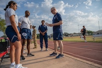 PT Trainer has his clipboard and is talking to a group of Airman who are about to take their PT test. Photo is outside on running track.