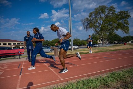 Airman is encouraged by trainer to finish his run on the track. Other trainers standing by and observing him finish the race.