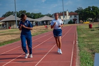 Trainer runs on the track in front of Airman coaching her and encouraging her to finish her run.