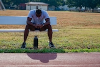 Airman sitting on bench outside the track at JBSA-Randolph. His head is down and he is taking a break after running.