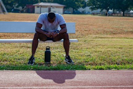 Airman sitting on bench outside the track at JBSA-Randolph. His head is down and he is taking a break after running.