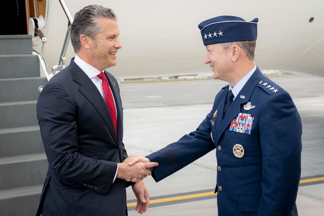 The defense secretary and the chairman of the Joint Chiefs of Staff shake hands in front of an aircraft.