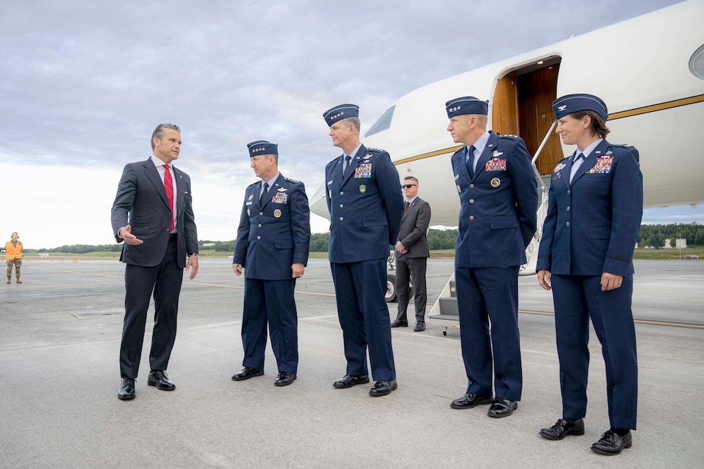 Five people stand on a tarmac in front of an aircraft on a gloomy day.