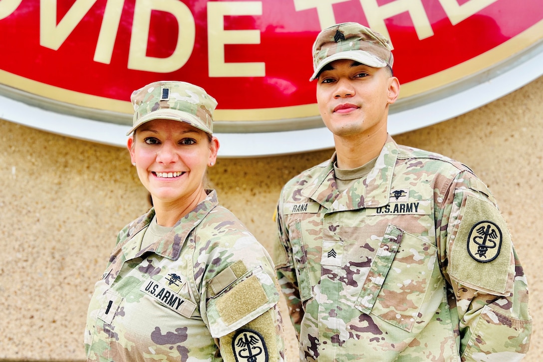 Two soldiers smile in front of a wall.