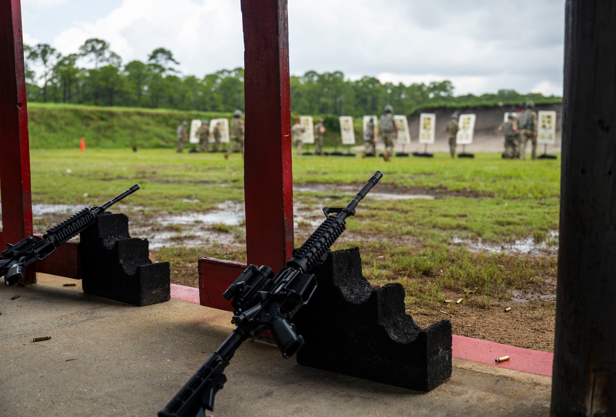Two M4 Carbines are rested at a range while a group of Airmen check their targets.