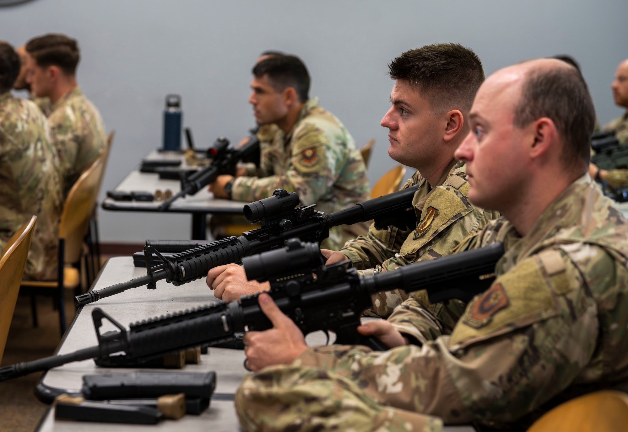 A row of Airmen hold a firearm in their hands.