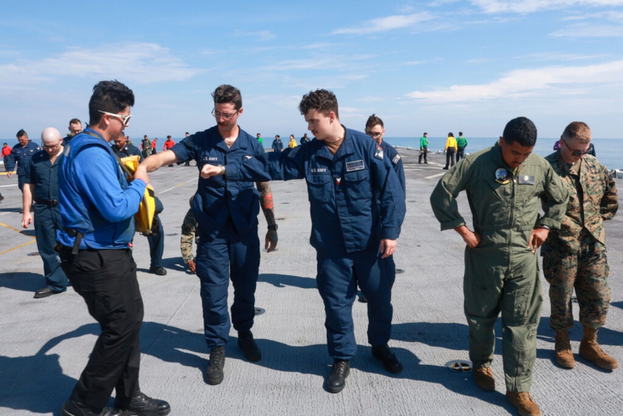 People wearing military uniforms of the Navy and Marine Corps look down as they walk along the deck of a ship searching for debris.