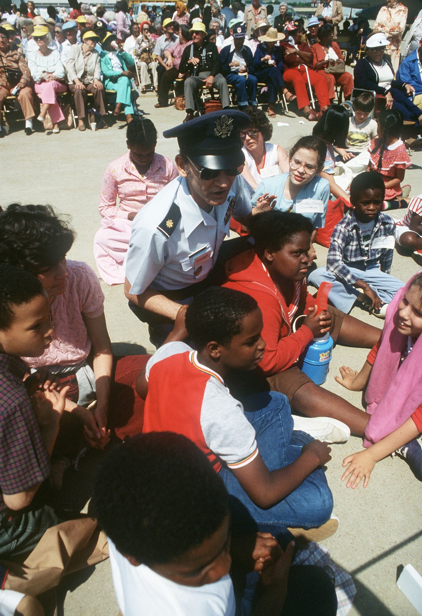 A U.S. Air Force major sits with a group of children attending the Joint Service Open House at Andrews Air Force Base, Maryland, May 13, 1983.