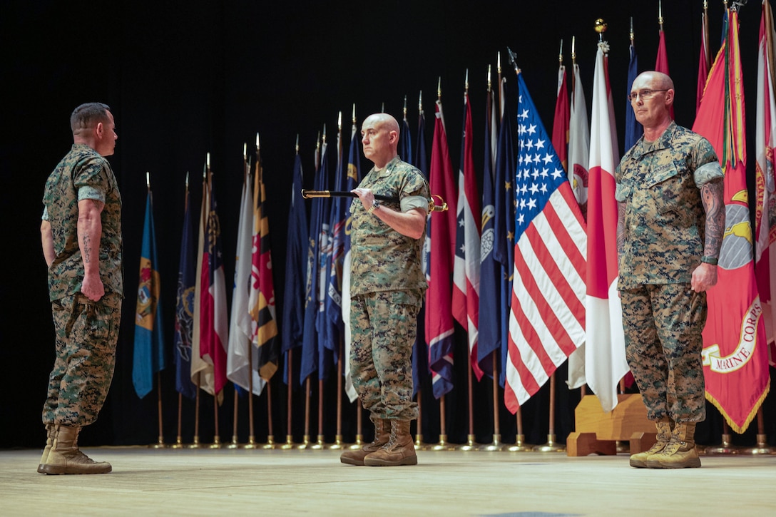 U.S. Marine Corps Col. Kenneth Rossman, center, the commanding officer of Marine Corps Air Station Iwakuni, and a native of Pittsburgh, Pennsylvania, prepares to pass the noncommissioned officer sword to Sgt. Maj. Richard Johnson, left, the oncoming sergeant major of MCAS Iwakuni, and native of Washington D.C., during a post and relief ceremony at MCAS Iwakuni, Japan, August 15, 2025. Post and relief ceremonies are a tradition that represents the transfer of responsibility, authority, and accountability from one sergeant major to another. (U.S. Marine Corps photo by LCpl. Maikeyla Reyes)