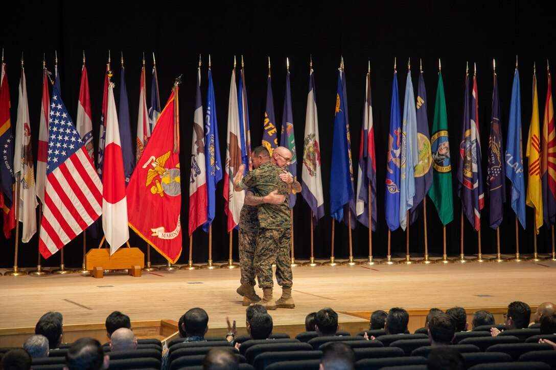 U.S. Marine Corps Sgt. Maj. Jody Armentrout, left, the outgoing sergeant major of Marine Corps Air Station Iwakuni, and native of Cedar Park, Texas, hugs Sgt. Maj. Richard Johnson, the oncoming sergeant major of Marine Corps Air Station Iwakuni, and native of Washington D.C., during a post and relief ceremony at MCAS Iwakuni, Japan, August 15, 2025. Post and relief ceremonies are a tradition that represents the transfer of responsibility, authority, and accountability from one sergeant major to another. (U.S. Marine Corps photo by Sgt. Randall Whiteman)
