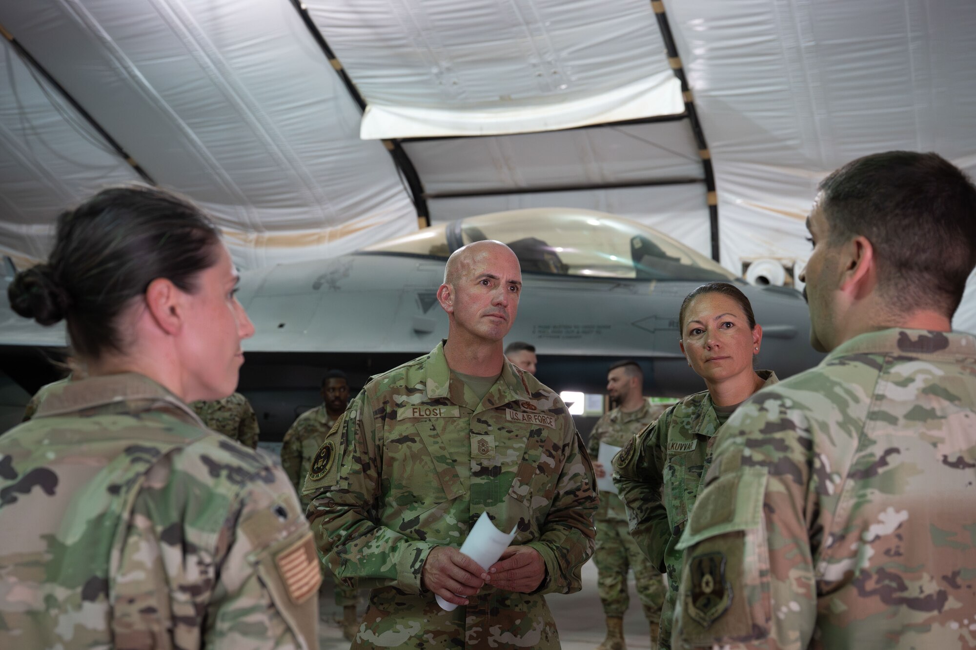 A group of people talk in front of an F-16 Fighting Falcon.