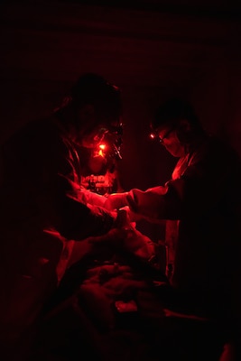 Cmdr. Paul Lewis (left), general surgeon, and Hospitalman Sebatiano Garofalo (right), surgical technologist, Expeditionary Resuscitative Surgical System (ERSS) 4, perform a simulated surgical procedure under red-light conditions, maintaining night-vision discipline while managing a combat casualty during an ERSS training conducted at Naval Expeditionary Medicine Warfighter Development Center (NEMWDC), June 9-17, 2025. Enlisted Sailors play a crucial role in the ERSS team, working closely with medical officers to deliver critical medical care in austere and high‑pressure environments. (U.S. Navy photo by Petty Officer 2nd Class Moira Esquivel)