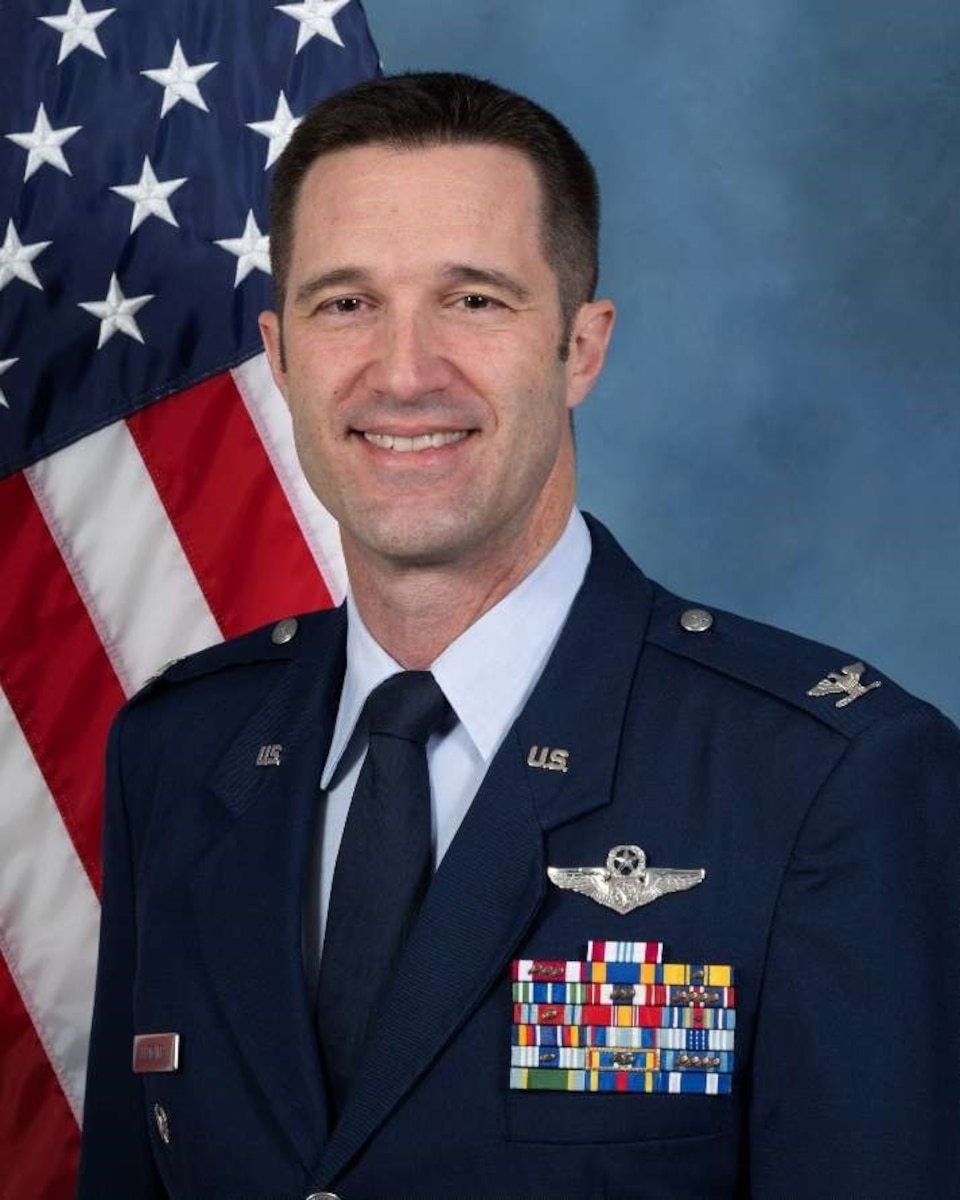 Man in military uniform smiling for official photo with U.S. flag in background