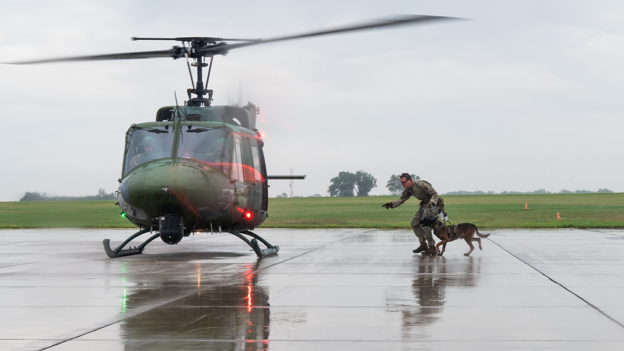 A U.S. Air Force military working dog handler and his dog run to board a helicopter in the rain.