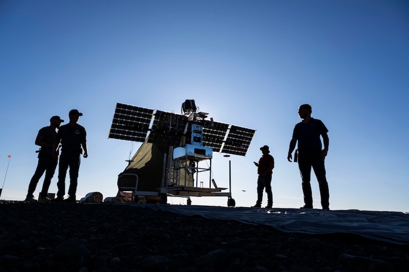 The silhouettes of four people are shown around a piece of equipment under blue skies.