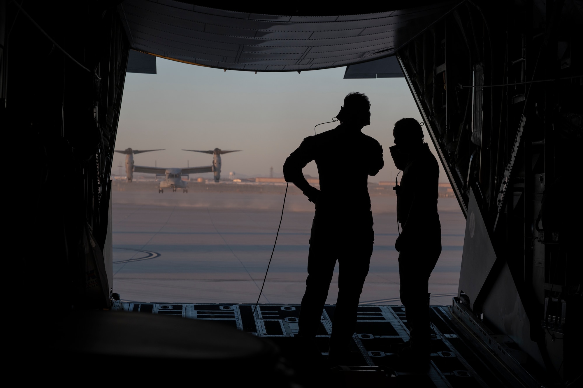 AFSOC Airmen watch a U.S. Marine Corps MV-22 hover behind a MC-130J Commando II during Emerald Warrior 25.2.