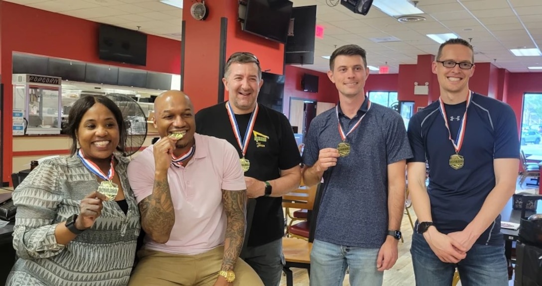 Four men and a lady hold gold medals.