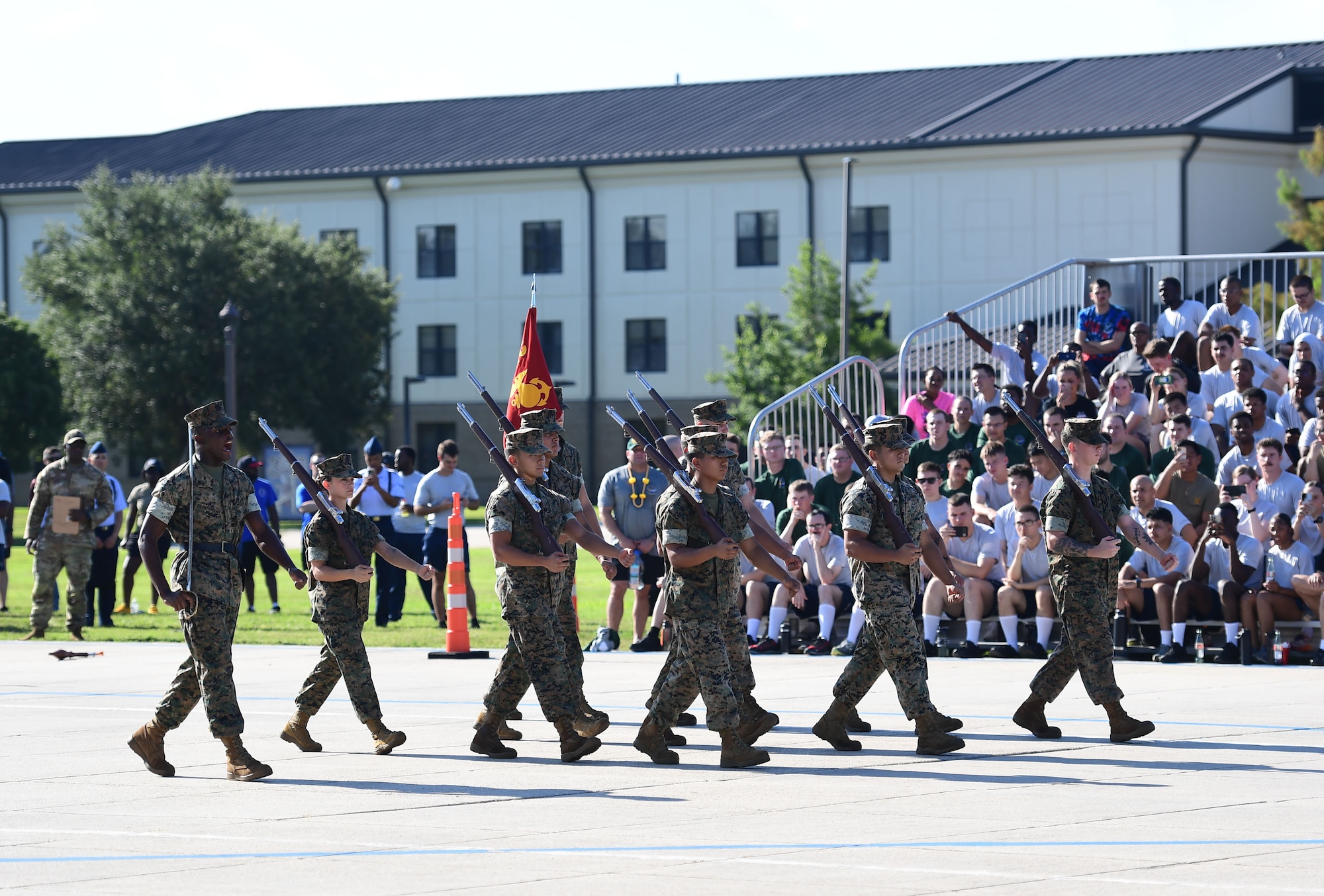A group of people wearing military uniforms march in formation in front of a crowd.