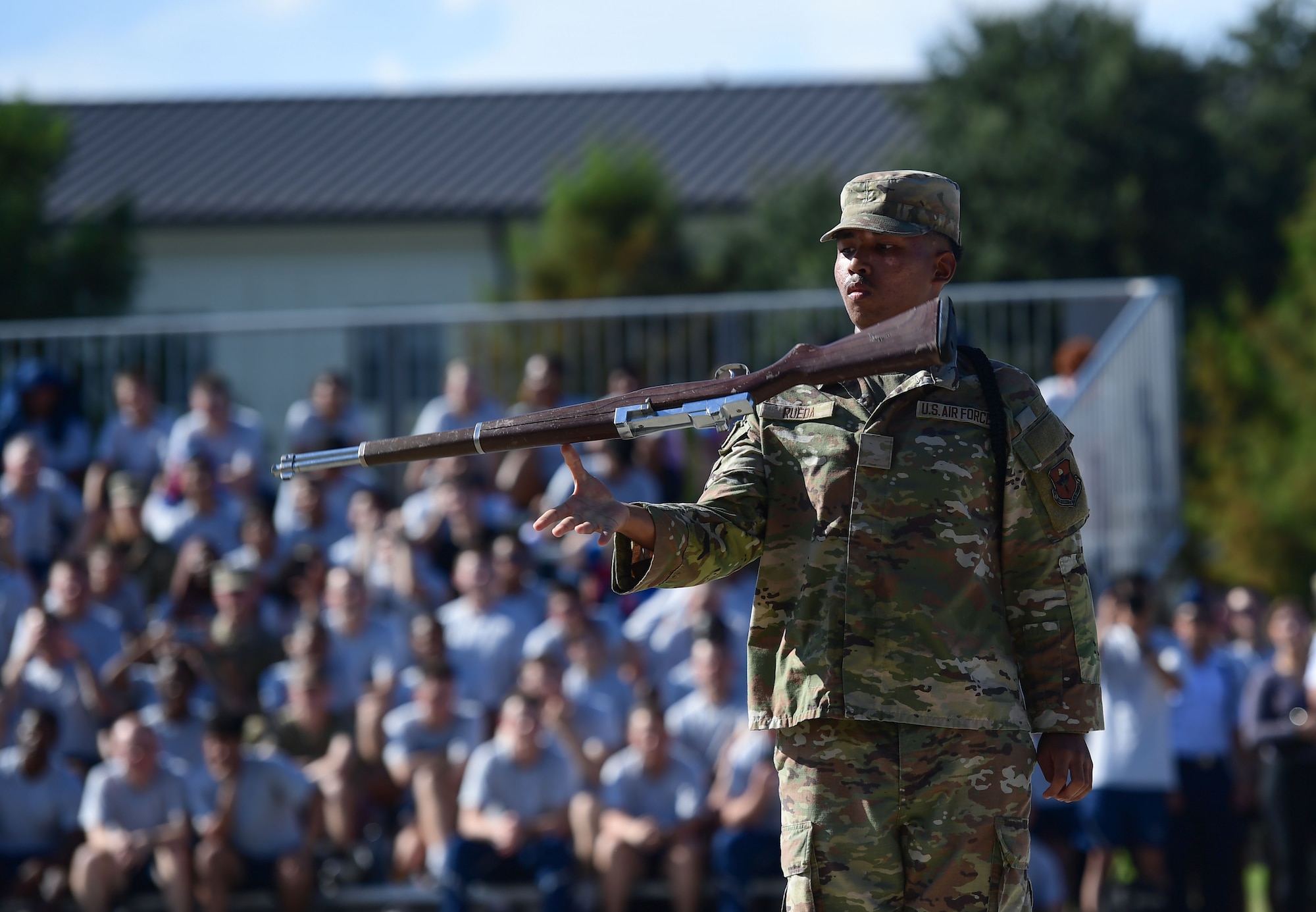 A man in military uniform spins a fake rifle in the air.