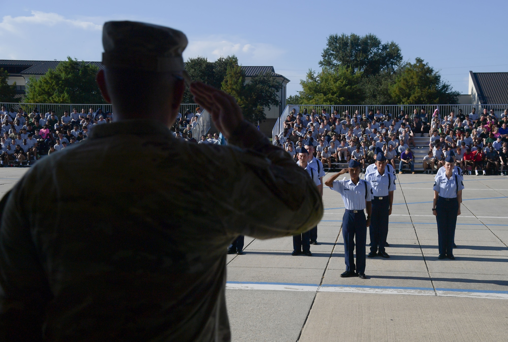 A man in uniform returns a salute to a group of people in military uniform.