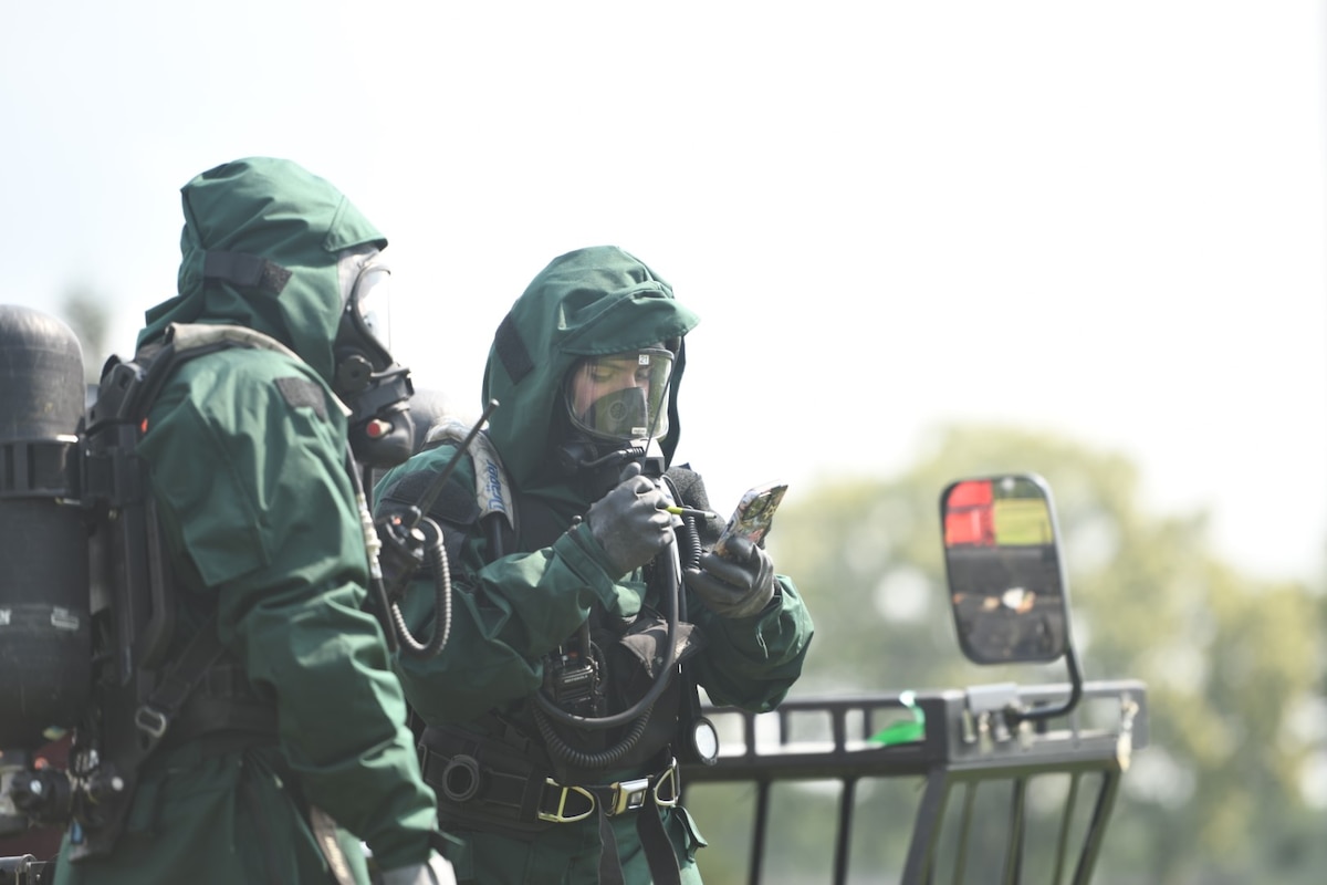 U.S. Army Spc. Gordon Trotman, member of the New Jersey National Guard’s 21st Weapons of Mass Destruction–Civil Support Team, left,  observes as Spc. Andrew DeJesus, also with the 21st WMD-CST, uses his phone to communicate with team members during a joint training exercise at Mercer County Park, West Windsor Township, New Jersey, July 31, 2025.