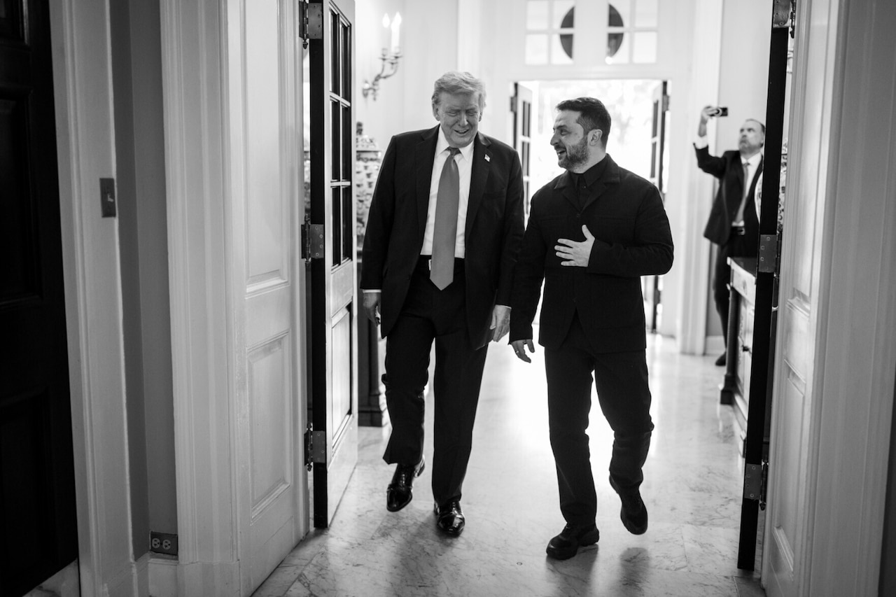 Two men wearing business attire smile and talk as they walk together through a doorway.