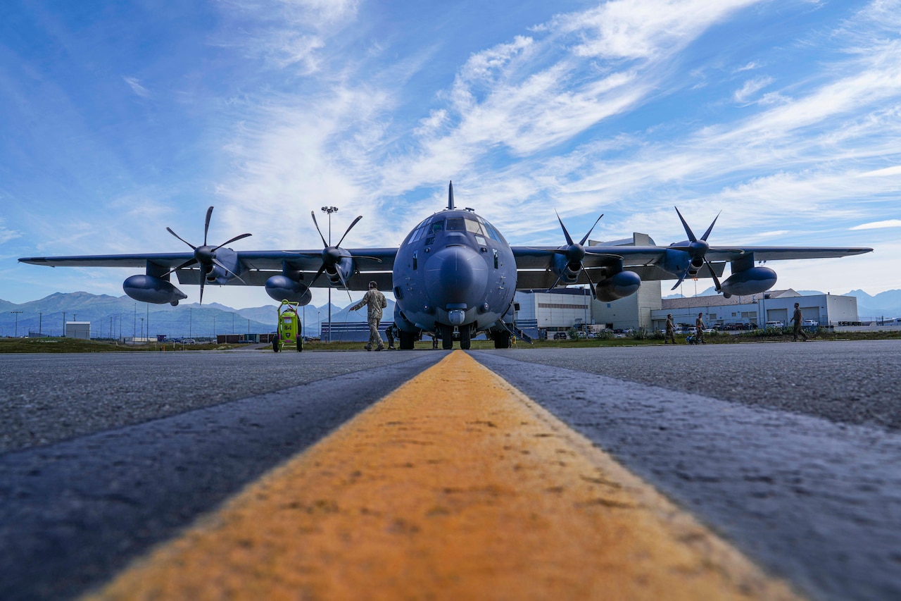 Airmen walk around a large aircraft on a runway outside under a partly cloudy sky as seen from the ground.