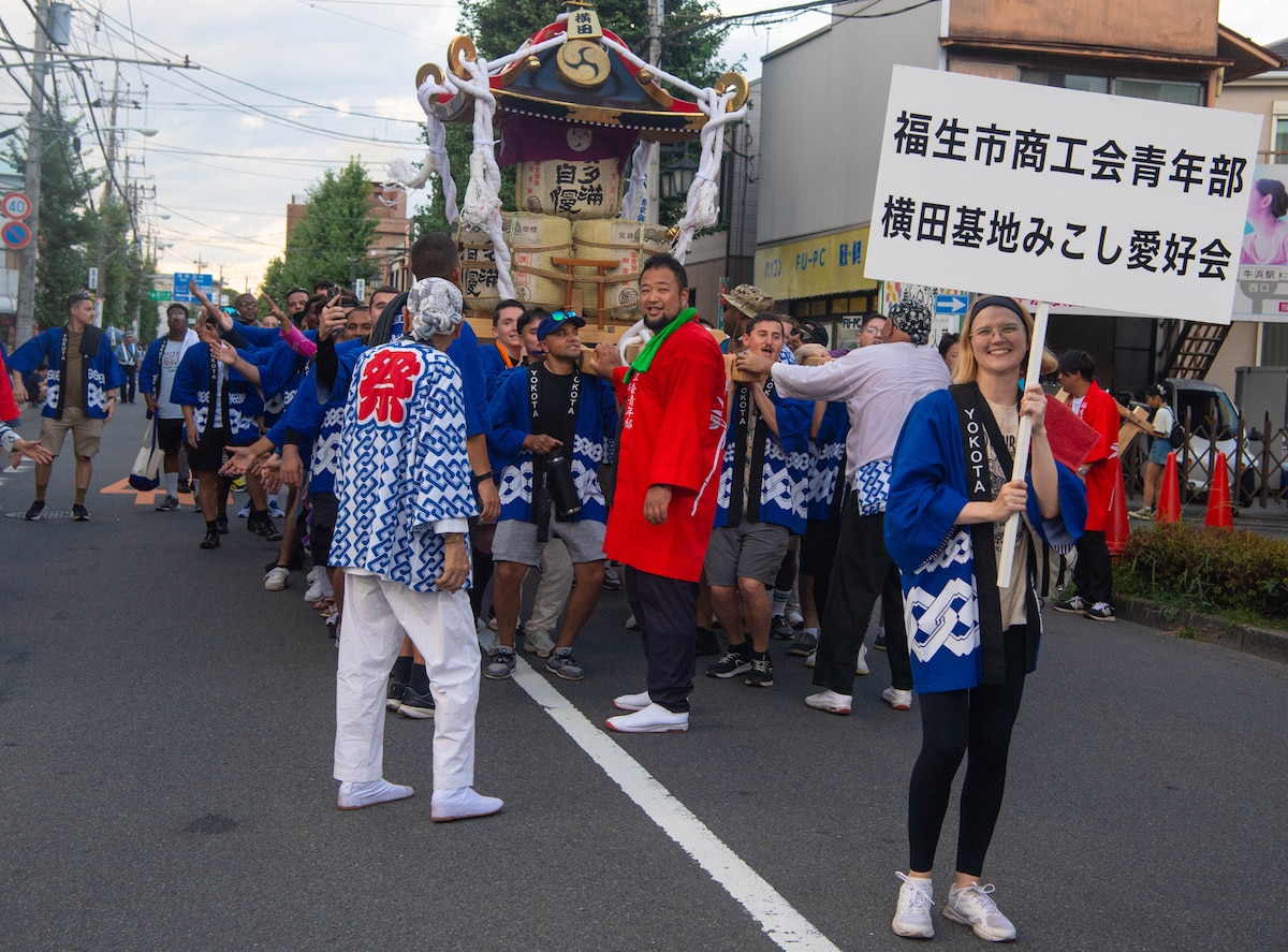 A woman carries a sign in front of a mikoshi.