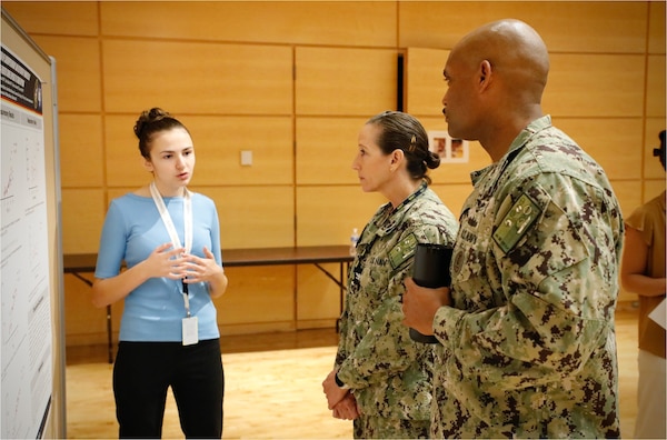 SILVER SPRING, Md. (Aug. 12, 2025) An intern at Naval Medical Research Command (NMRC) discusses research undertaken during the summer alongside Navy scientists with Capt. Franca Jones, Commander, NMRC, and Master Chief Hospital Corpsman Phillip Jean-Giles, command master chief for NMRC. NMRC, headquarters of Navy Medicine Research & Development, is engaged in a broad spectrum of activity from basic science in the laboratory to field studies in austere and remote areas of the world to investigations in operational environments. In support of Navy, Marine Corps and joint U.S. warfighter health, readiness and lethality, researchers study infectious diseases, biological warfare detection and defense, combat casualty care, environmental health concerns, aerospace and undersea medicine, operational mission support and epidemiology. (U.S. Navy Photo by Sidney Hinds/ released)