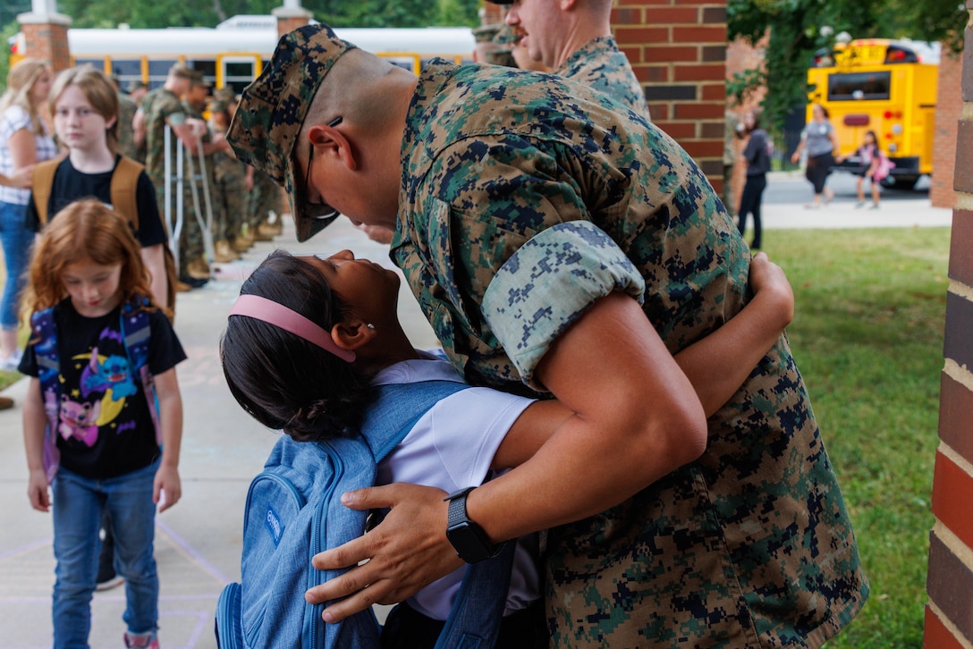 U.S. Marine Corps Gunnery Sgt. George M. Ward, a data systems chief with Marine Corps Cyberspace Operations Group, hugs his daughter as he welcomes her to her first day of school during a back-to-school celebration at the Crossroads Elementary School on Marine Corps Base Quantico, Virginia, Aug. 18, 2025. This event welcomed students back to the classrooms, strengthening the bonds between the Marines and the MCB Quantico community. (U.S. Marine Corps photo by Lance Cpl. Donovan E. Melendez)