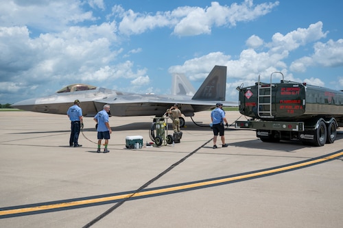 four men stand while a plane gets fueled up