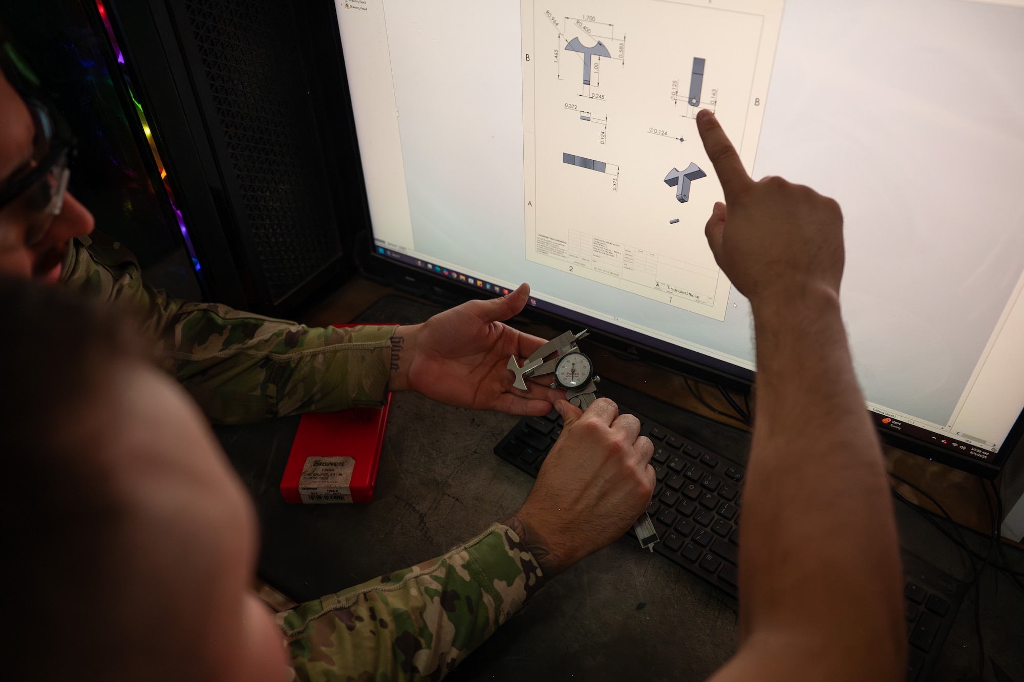 Two Airmen point at an aircraft part on a computer monitor