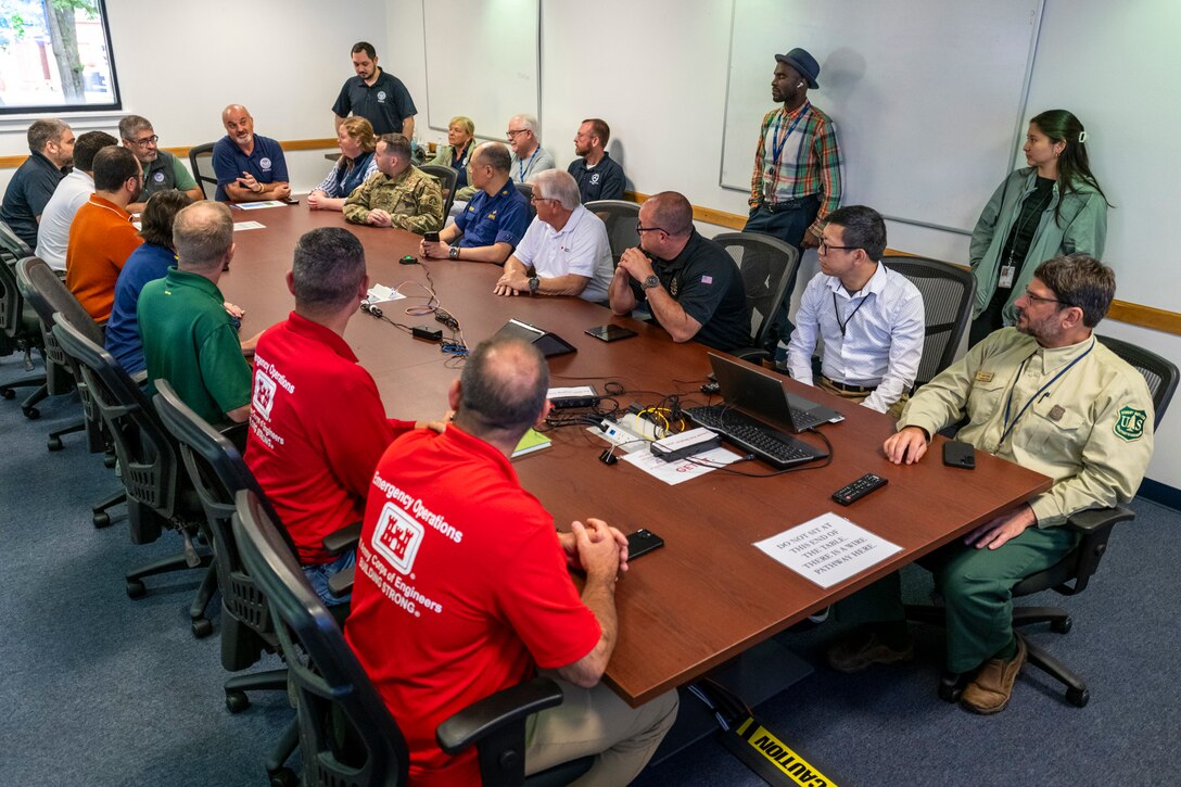 More than 20 people gather around a conference table for a meeting.