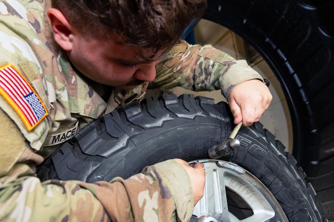 A soldier is shown repairing a tire with a small instrument as seen from close up.