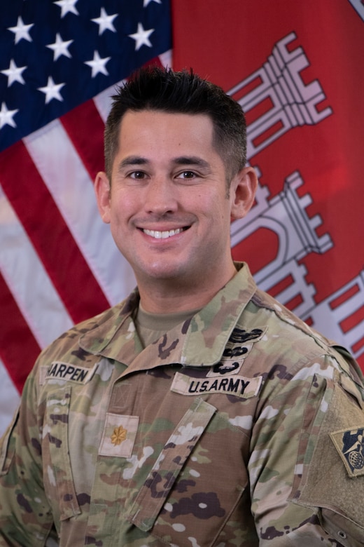 Soldier in fatigues in front of American and engineer flags