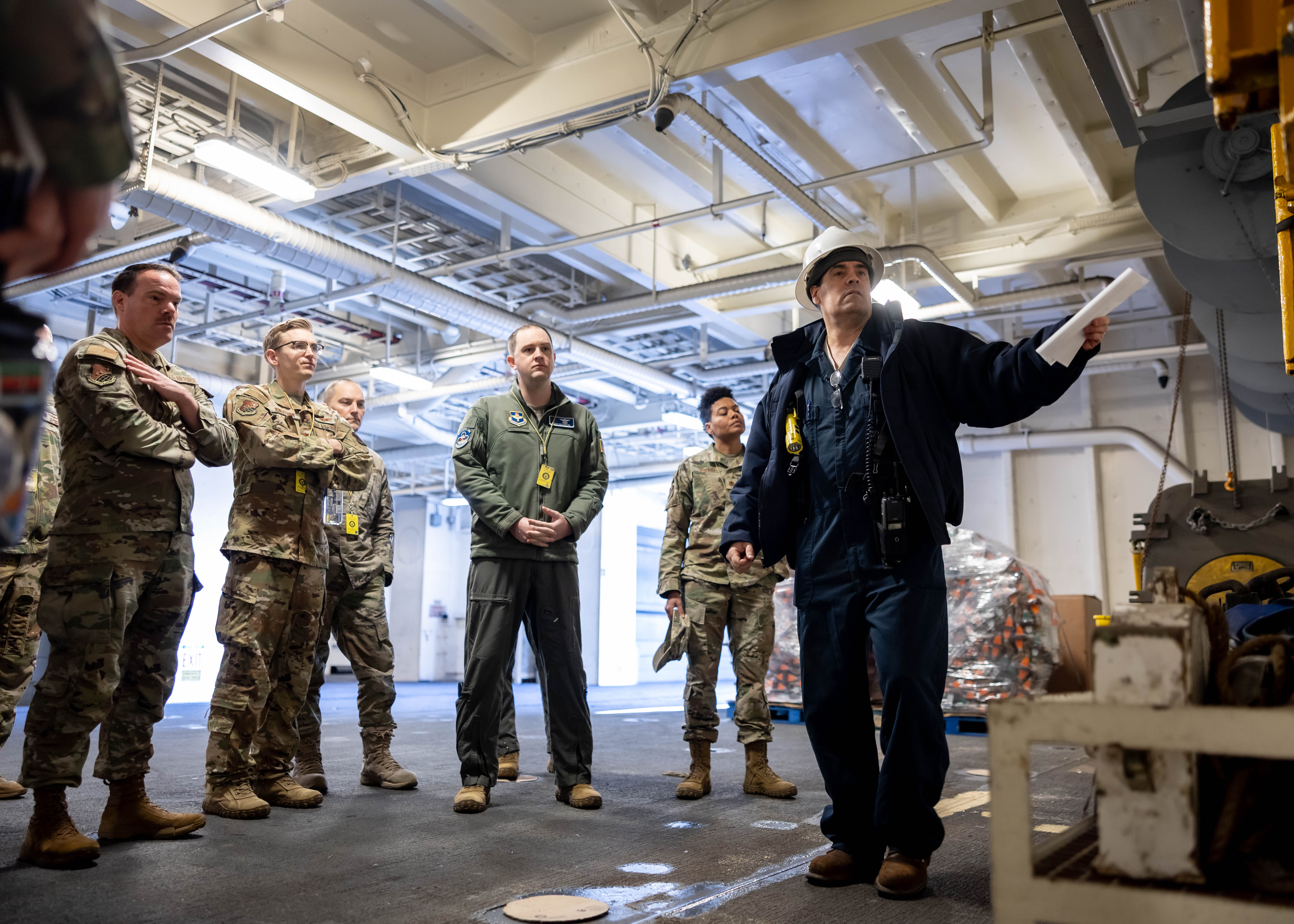 Joseph Flatley, Chief Mate, USNS William McLean (T-AKE 12), briefs members of the Advanced Study of Air Mobility (ASAM) course on the equipment used in a replenishment at sea evolution during a tour of the ship March 10, 2025. During the tour 14 Air Force Majors visited various areas of the ship to familiarize themselves on the ship and at-sea naval logistics.