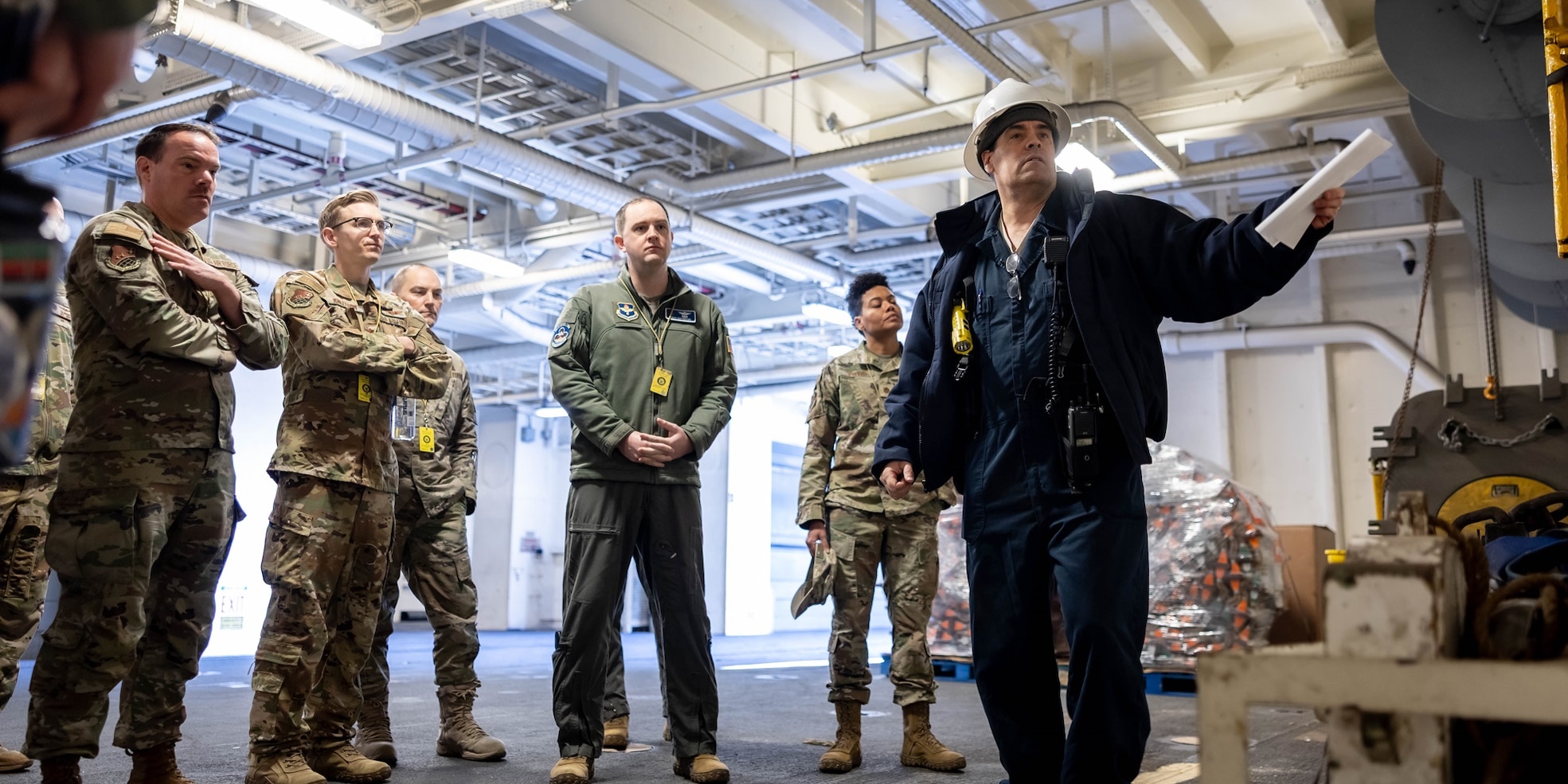 Joseph Flatley, Chief Mate, USNS William McLean (T-AKE 12), briefs members of the Advanced Study of Air Mobility (ASAM) course on the equipment used in a replenishment at sea evolution during a tour of the ship March 10, 2025. During the tour 14 Air Force Majors visited various areas of the ship to familiarize themselves on the ship and at-sea naval logistics.