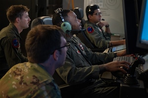 uniformed U.S. Airmen wearing headsets fly MQ-9 simulators