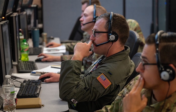 U.S. Air Force Airmen wearing headsets work at computers