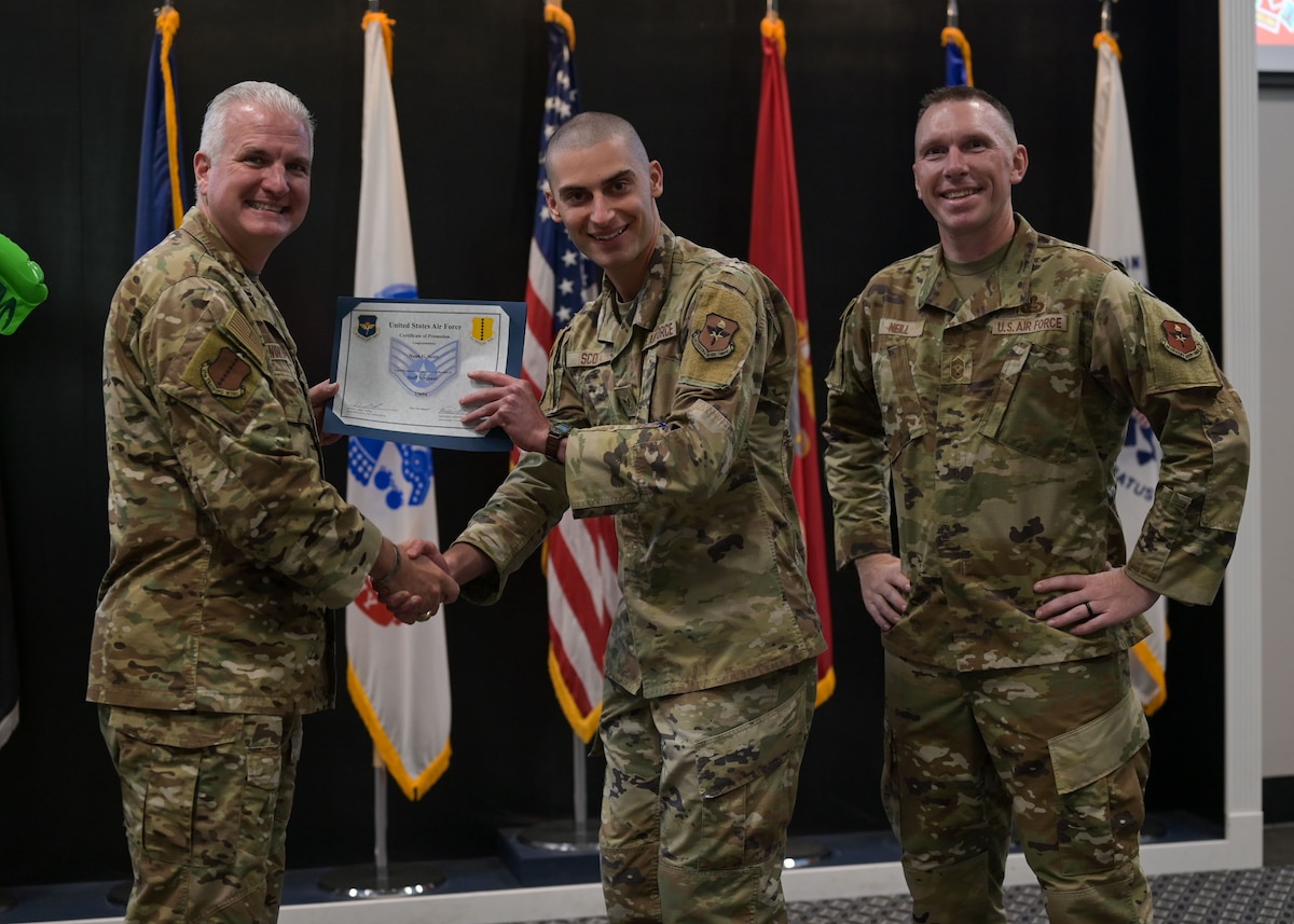 U.S. Air Force Col. Matthew Norton, 17th Training Wing commander and Chief Master Sgt. Derek Neil, 17th TRW command chief, present Senior Airman Noah Scott, 17th Medical Group optometrist specialist, with his Staff Sgt. select certificate at the 25E5 Staff Sgt. release party at the Powell Event Center, Goodfellow Air Force Base, Texas, Aug. 18, 2025. Staff sergeants are the backbone of the Air Force as the first rank of noncommissioned officers and the frontline supervisors who develop their subordinates, develop themselves further, and ensure proper use of resources under their control. (U.S. Air Force photo by Senior Airman Evelyn J. D’Errico)