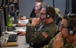 U.S. Air Force Airmen wearing headsets work at computers