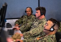 uniformed U.S. Sailors wearing headsets work at computers