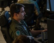 uniformed U.S. Airman wearing a headset flys a MQ-9 simulator