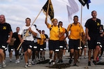 People in athletic attire run in formation with those in front holding flags.