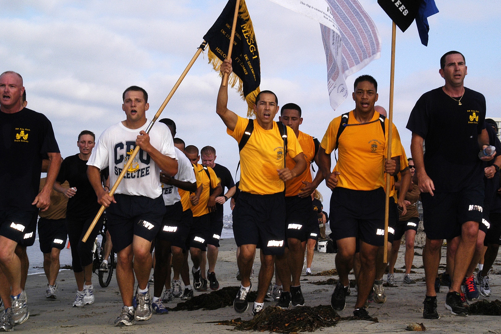 People in athletic attire run in formation with those in front holding flags.